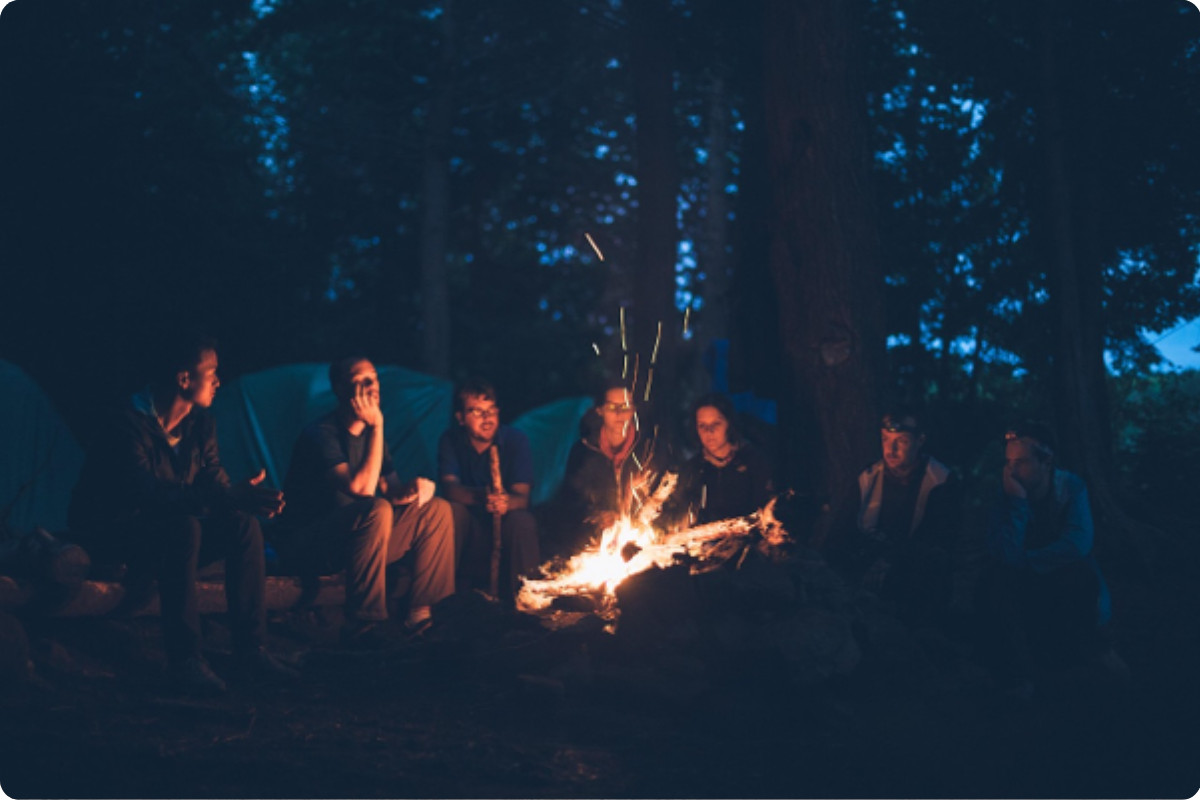 Familie die im Wald am Lagerfeuer sitzt.